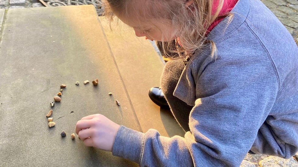 A child sitting outdoors arranging small stones in a curved pattern, focused and calm in warm autumn light.