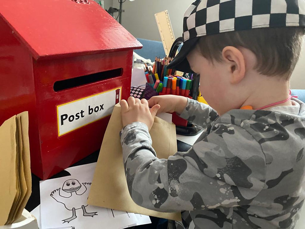A child posts an envelope into a red post box during a playful activity linked to early sounds and communication.