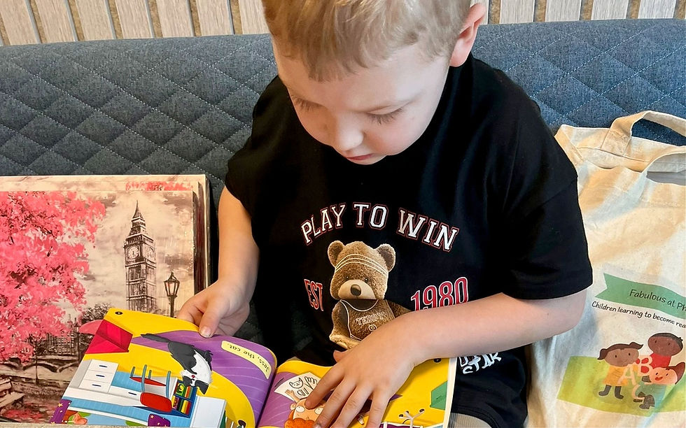Child sitting on a sofa reading a phonics book, with a Fabulous at Phonics tote bag beside them.