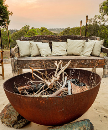 Outdoor fire pit with lounge behind it, relax by the fire at the luxury holiday house on the Coffs Coast.