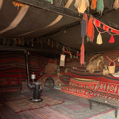 Image of the interior of a tent in Wadi Rum, Jordan, set up for a group gathering. The spacious and cozy tent is adorned with traditional Bedouin-style decor, including carpets, cushions, and low tables, creating a warm and inviting atmosphere for socializing and group activities in the beautiful desert surroundings of Wadi Rum.