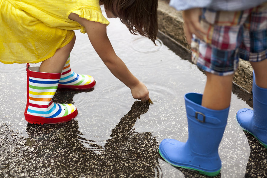 children in rainboots playing in a puddle
