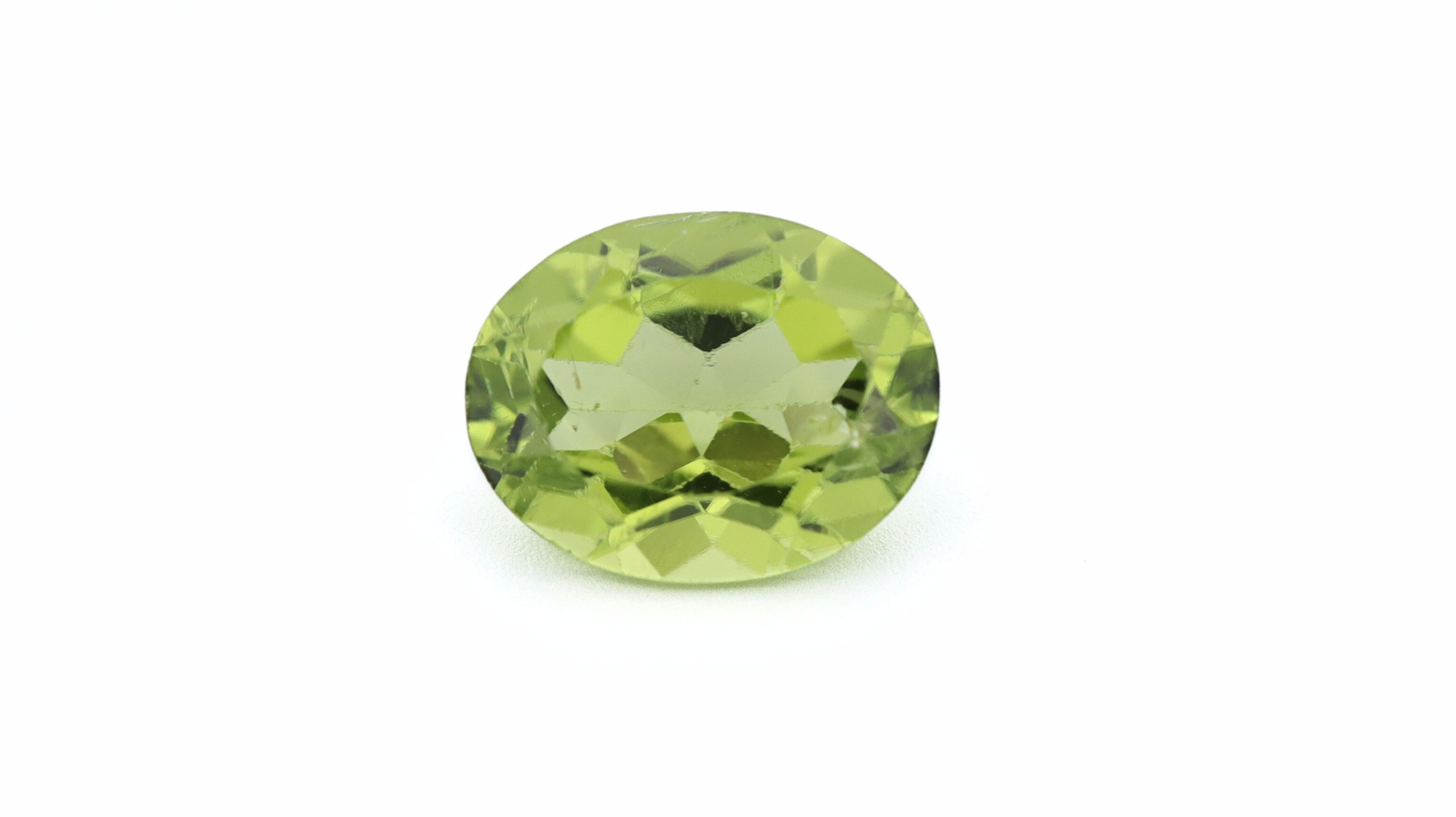 Front photo of a an oval cut Peridot, white background, 9x7mm, with very good color saturation and hue.