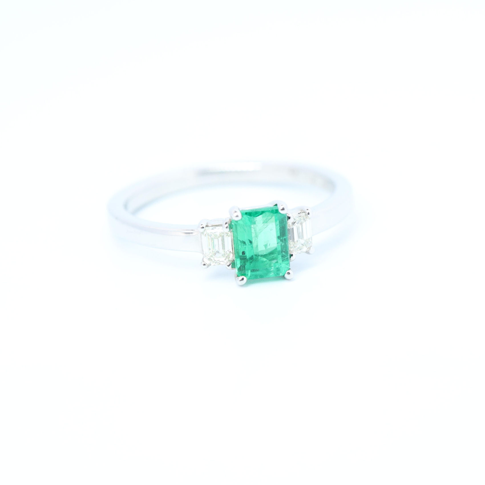 Photo of a ring with a central intense green emerald, adorned by 2 emerald cut diamonds, with the same L/W radio.