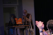 KSLF - Rahul Singh on stage, turned towaards the camera hands together in thanks. An audience member is seen in the bottom right corner from ears up, hands together in applause.
