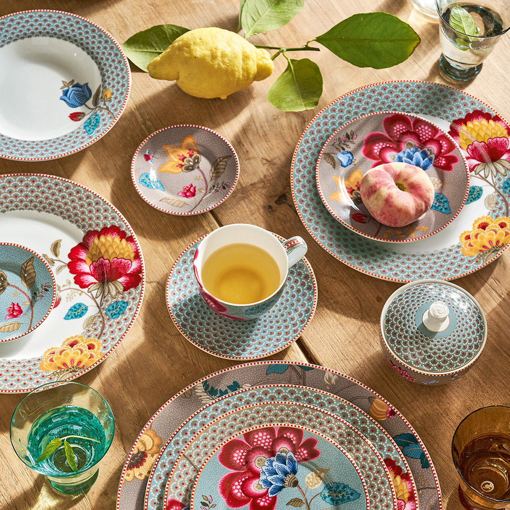 Mesa com peças Blooming Tales azul e cáqui em fotografia do catálogo brasileiro