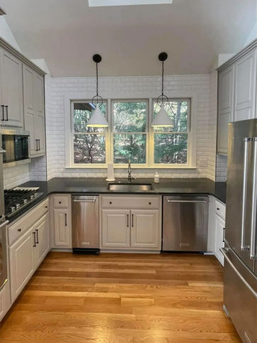Contemporary kitchen with white cabinetry, dark countertops, stainless steel appliances, subway tile backsplash, light wood flooring, minimalist pendant lights, and large windows.