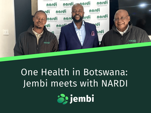 Three men smiling in front of a white "nardi" backdrop. Two wear black jackets; one is in a blue suit. Indoor setting with a tile floor. Title says One Health in Botswana: Jembi meets with NARDI