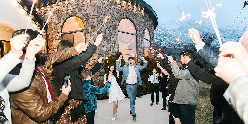 Couple leaving their wedding with snowy mountains in the background, family sending them off with sparklers.