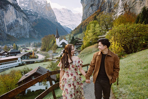 Couple photoshoot in Lauterbrunnen, Switzerland: two people holding hands on a path above the valley with autumn colors and snow-capped mountains.