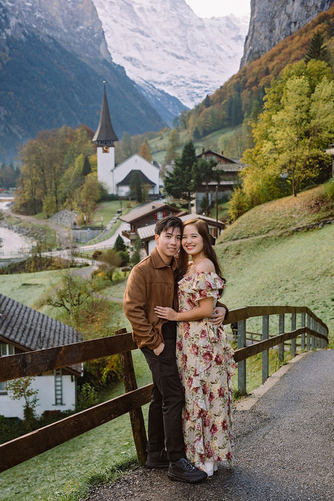 Couple photoshoot in Lauterbrunnen Valley, Switzerland, hugging on a path with the church and snowy mountains in the background.