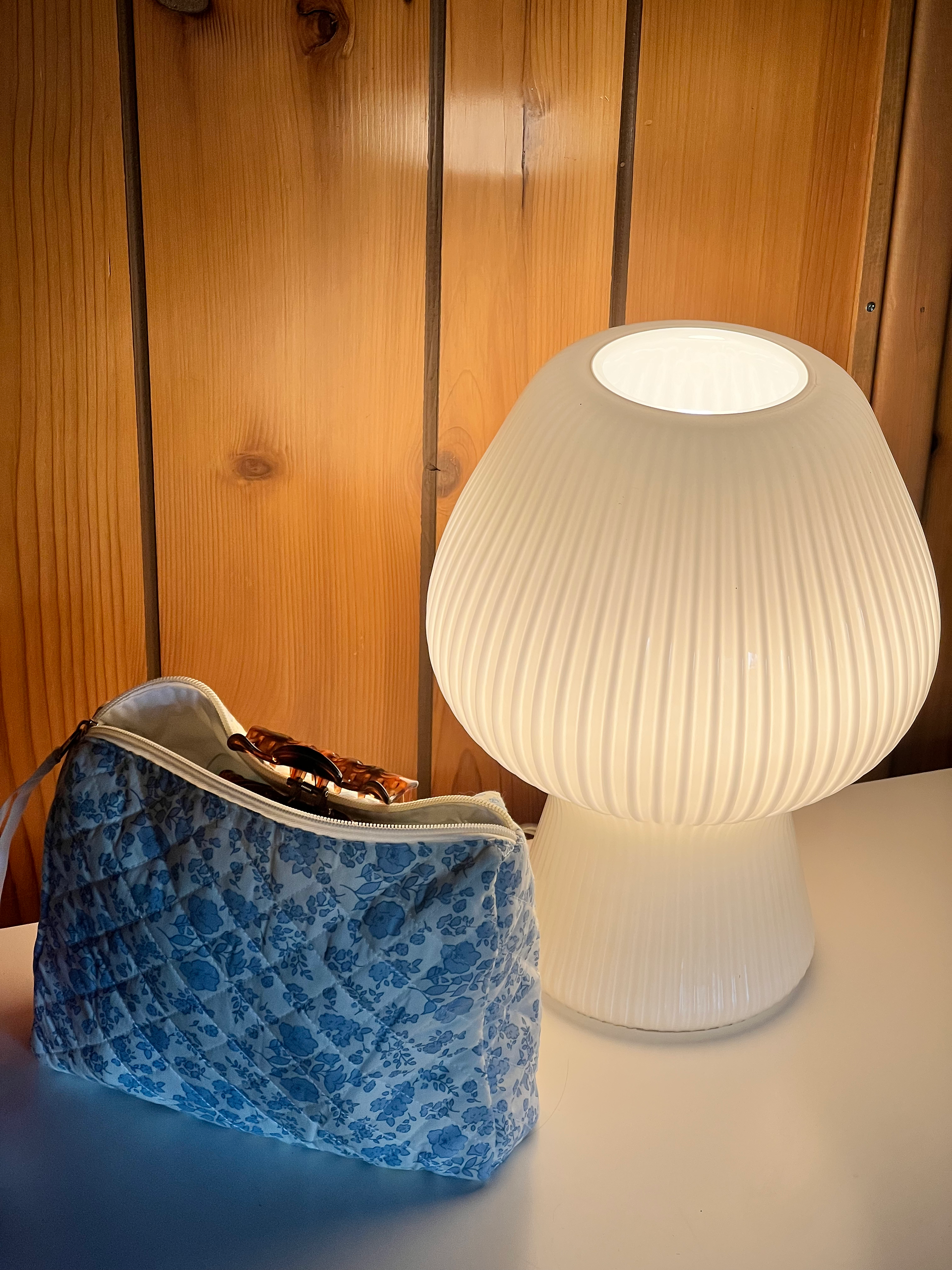 Blue and white floral cosmetic bag with a brown hair clip hanging off of it, next to a modern white lamp.