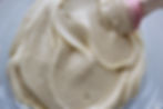 Close-up of creamy, smooth coconut pastry cream in a bowl, mixed with a pink spatula. The pastry cream is light beige with a glossy texture.