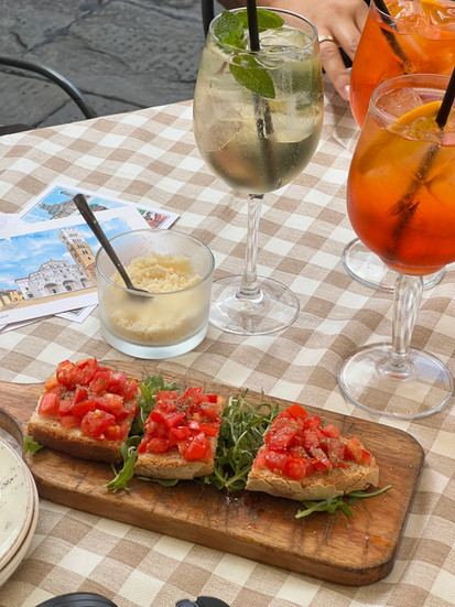 bruschetta on wood cutting board with parmesan and two aperol sprtiz and a hugo spritz
