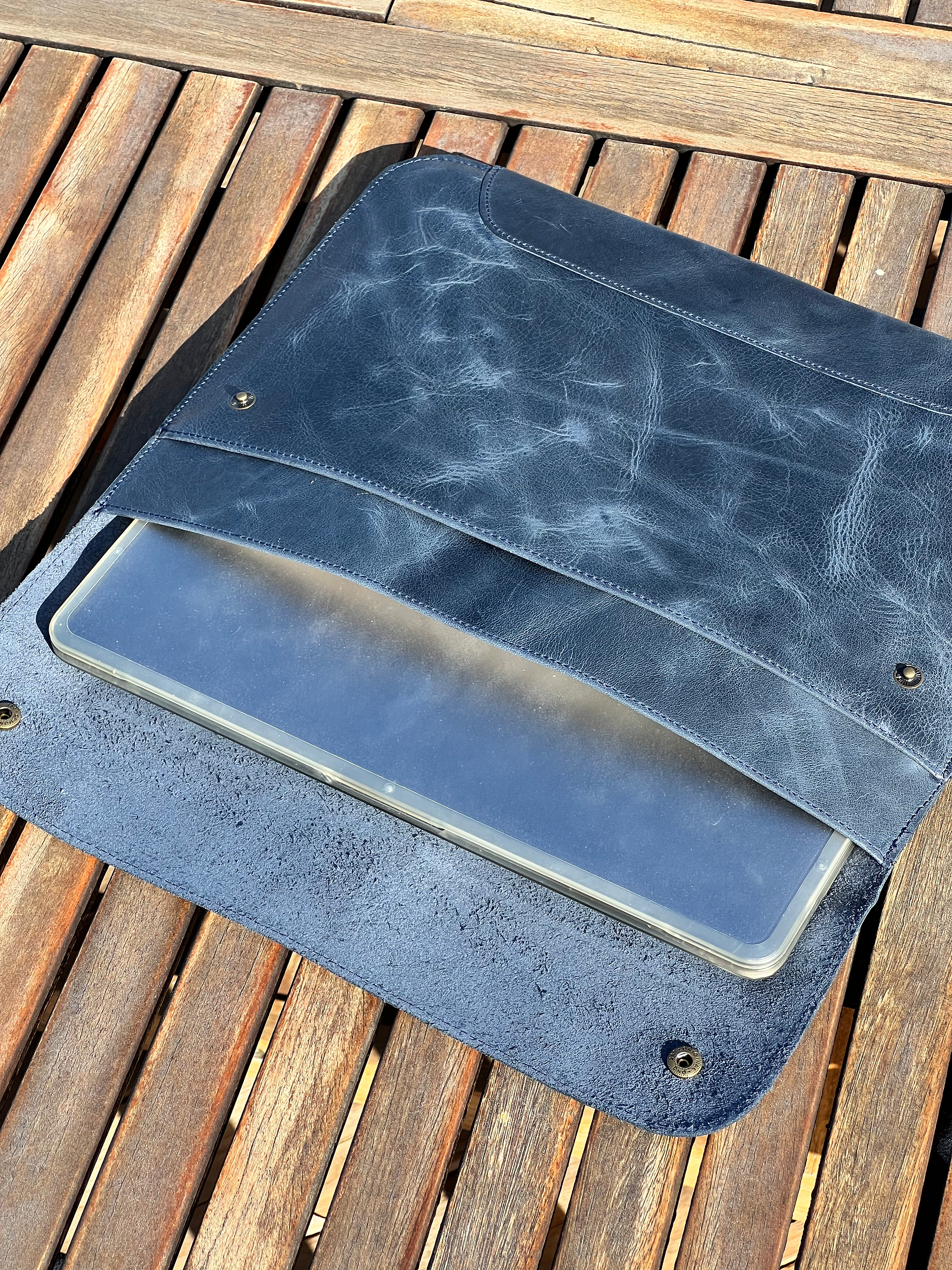 an opened blue leather laptop case on a wooden table with the macbook peeking out