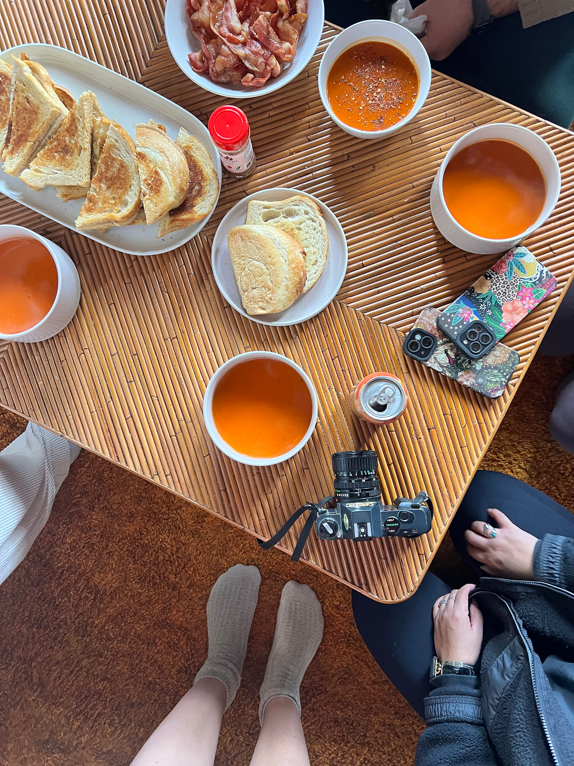 Spread of grilled cheese and tomato soup on a bamboo coffee table with iphones and film camera.