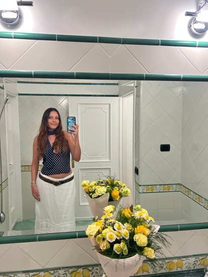 white and blue polka dot tank with white skirt and belt mirror selfie in front of yellow flowers