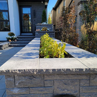 A flower bed made of black limestone with a modern home in the background