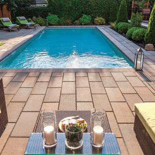 A large rectangular pool in a backyard surrounded by a large patio and trees