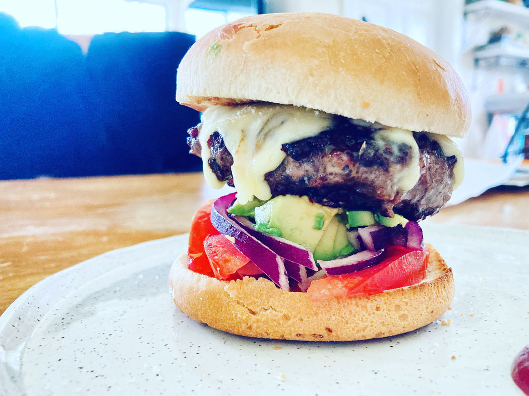 Gourmet burger with avocado, melted cheese, tomato, and red onion on a ceramic plate, hawaii