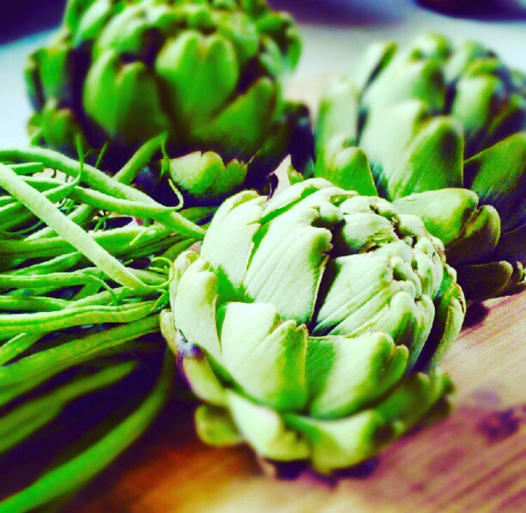 Three whole fresh artichokes with stems on a purple surface