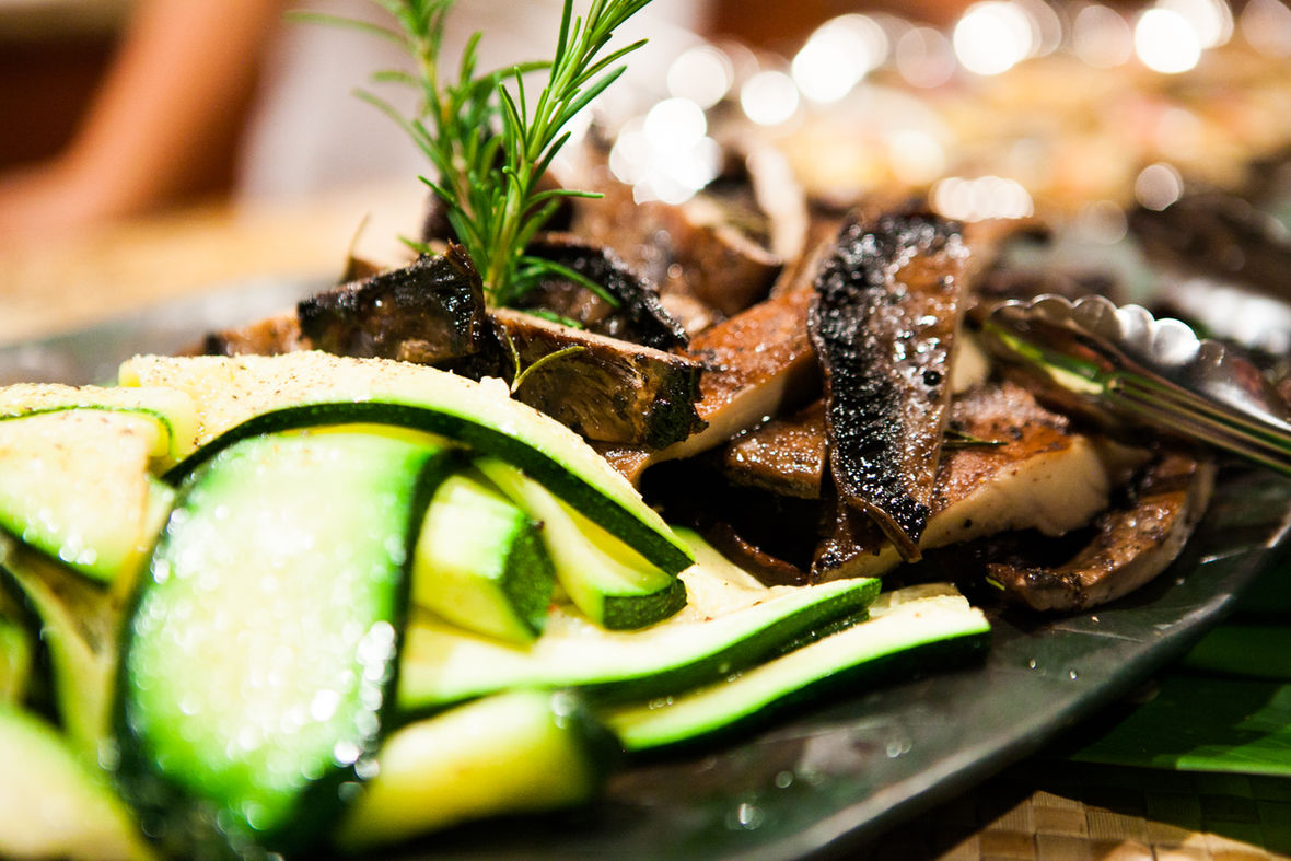 Sautéed mushrooms and zucchini ribbons with a rosemary sprig on a dark plate, Big Island