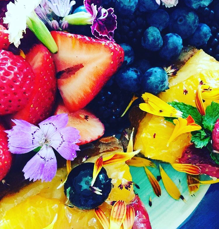 Bowl of fresh strawberries, blueberries, orange slices, and edible purple and yellow flowers, hawaii