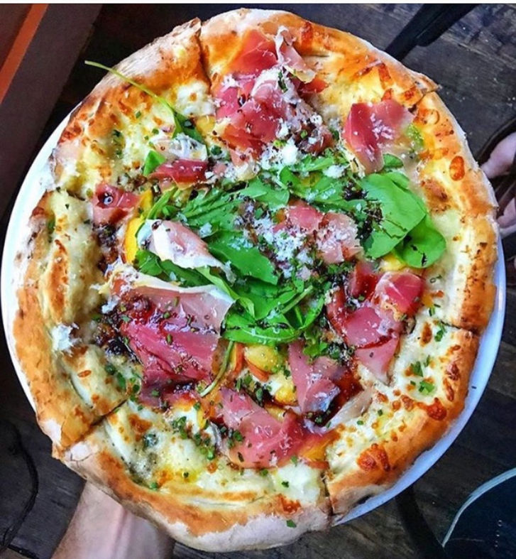 Thin-crust pizza topped with prosciutto, arugula, and fresh herbs