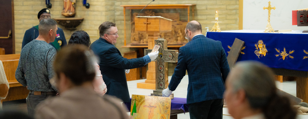 Hombres con guantes blancos presentan una cruz reliquiario sobre un altar mientras fieles observan dentro de una iglesia.