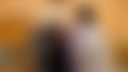 Sacerdote en sotana blanca aplica ceniza en la frente de una mujer en una iglesia de ladrillo. Fila de personas espera su turno. Atmosfera solemne.