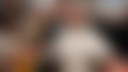 Un clérigo sonriente en túnica blanca saluda a una multitud en una iglesia grande. Personas toman fotos; ambiente alegre y colorido.