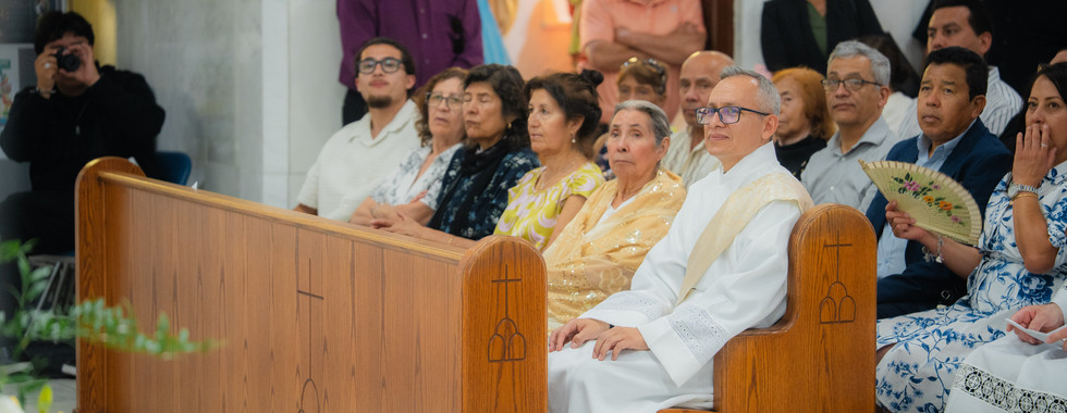 Deacon in white vestments sits in a church pew with seated congregants, some holding fans, in a solemn service.