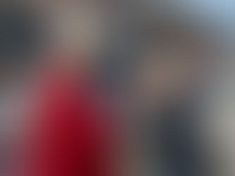 Un obispo con túnica roja y mitra bendice a una mujer que sostiene hojas. Fondo urbano con transeúntes desenfocados. Ambiente solemne.