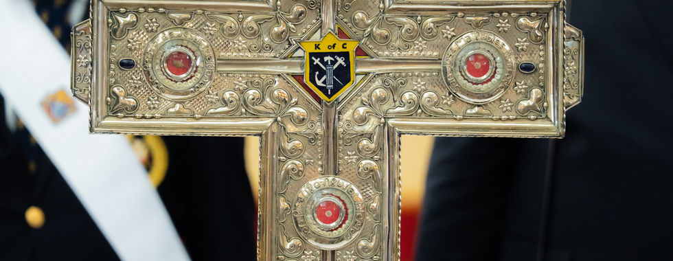 Cruz ornamentada con reliquias colocada sobre un altar, con miembros de una organización ceremonial de pie al fondo.