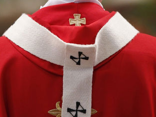 Primer plano de una vestidura roja de clérigo con estola blanca y cruces bordadas, sobre fondo desenfocado.