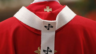 Primer plano de una vestidura roja de clérigo con estola blanca y cruces bordadas, sobre fondo desenfocado.