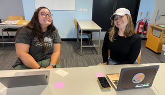 This is an image of 2 women smiling with their index cards and computers in front of them. They finished sharing their stories and are celebrating.