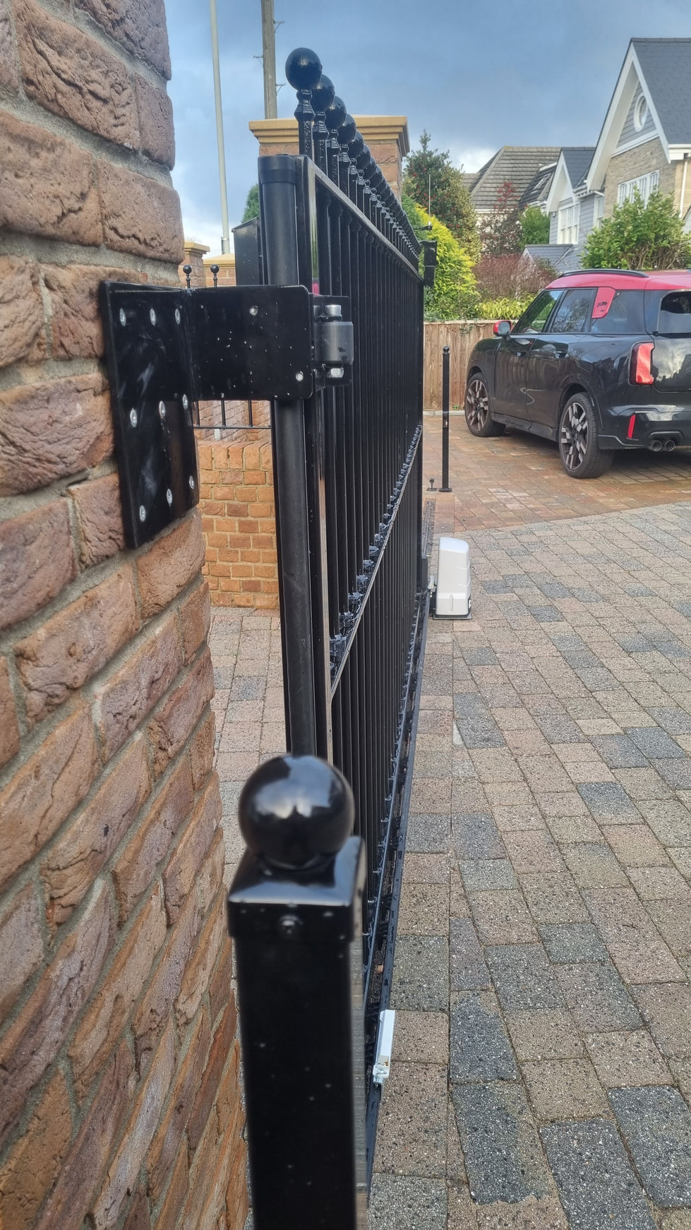Aluminium photocell safety post with decorative ball-top cap beside automated sliding gate