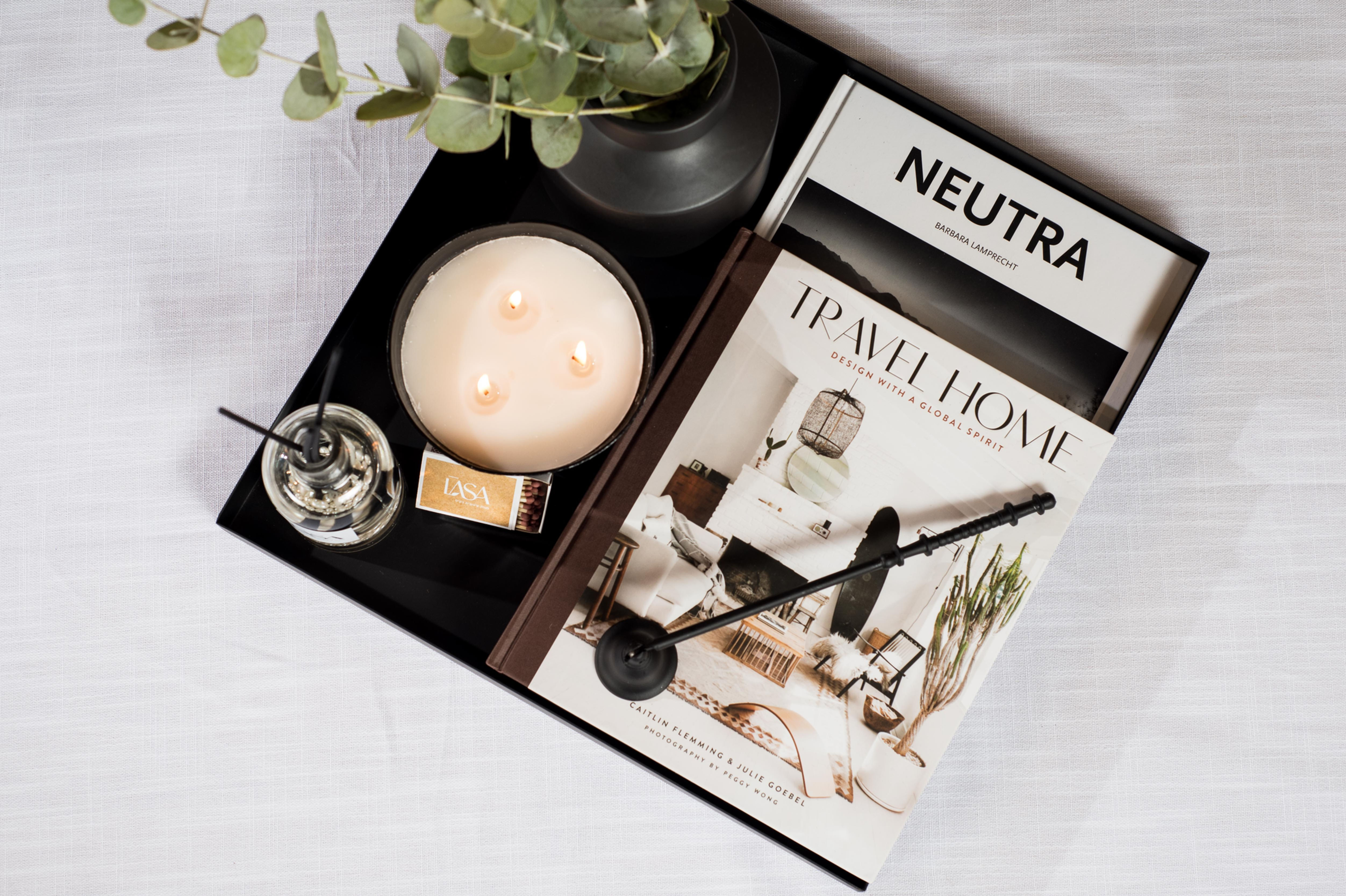 בתמונה מופיע מגש מידה 38 ס"מ*38 ס"מ ו2 ספרי עיצוב, פעמון כיבוי נר, נר עגול שחור עם 3 פתילים, דיפיוזר בבקבוק זכוכית ואגרטל עם