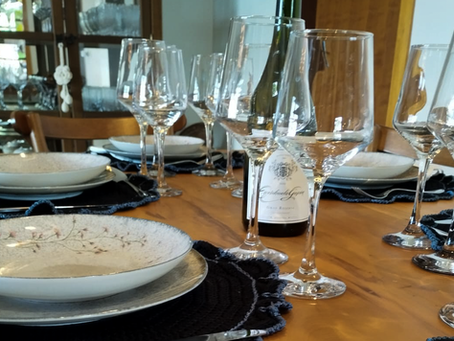 foto contém pratos, taças e um ótimo vinho de qualidade sobrepostos sobre uma mesa.