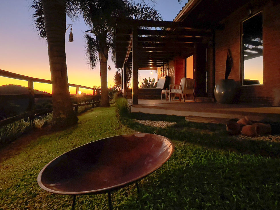 Foto do nascer do sol, com a vista da varanda e logo a frente um objeto para fazer uma fogueira