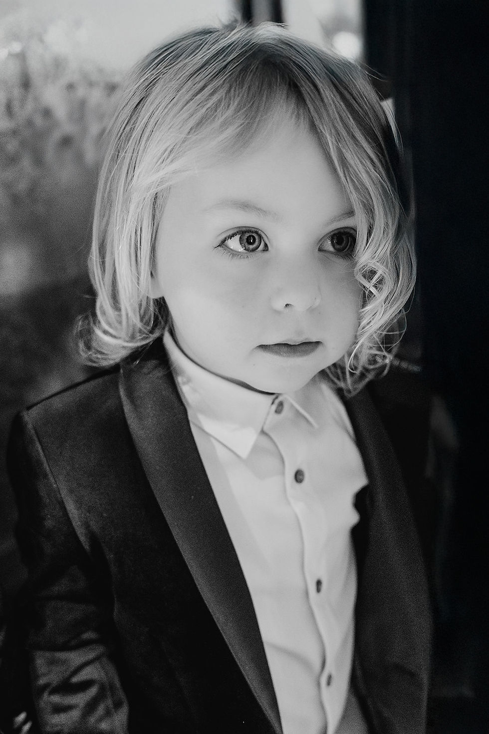 Young child in a suit, gazing thoughtfully, with wavy hair. The monochrome setting adds a timeless, contemplative feel.