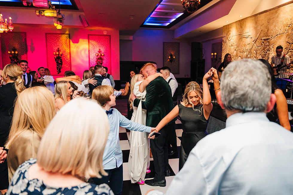 People dance joyfully in a warmly lit venue with checkered floor and vibrant red walls. A couple embraces, enhancing the festive mood.