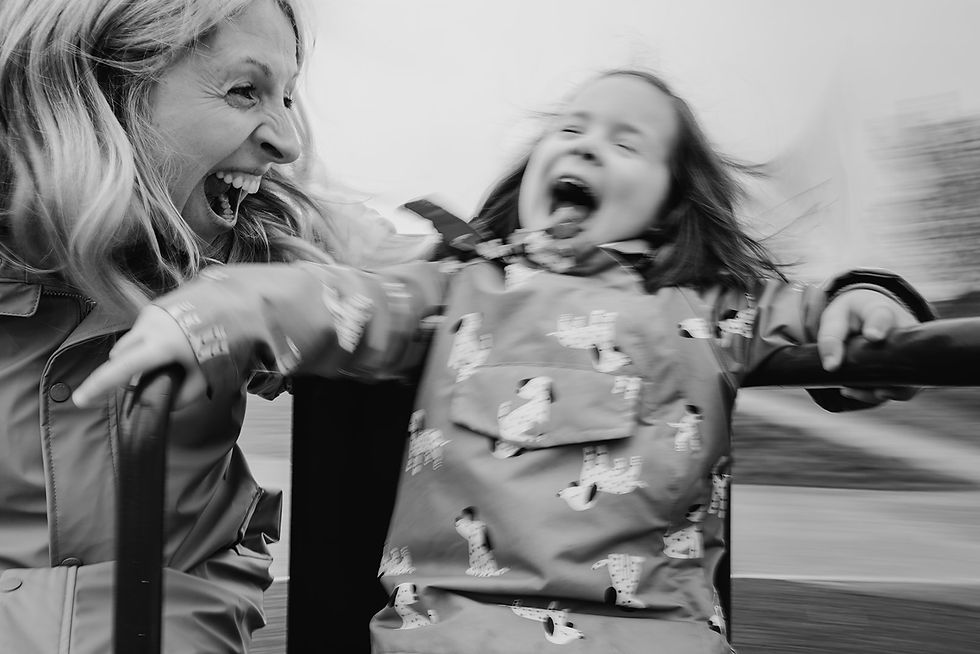 Woman and child laughing joyfully on a carousel. The child wears a patterned jacket. Motion blur adds excitement. Black and white image.