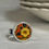 Thumbnail: small round ring with yellow flower on an orange background