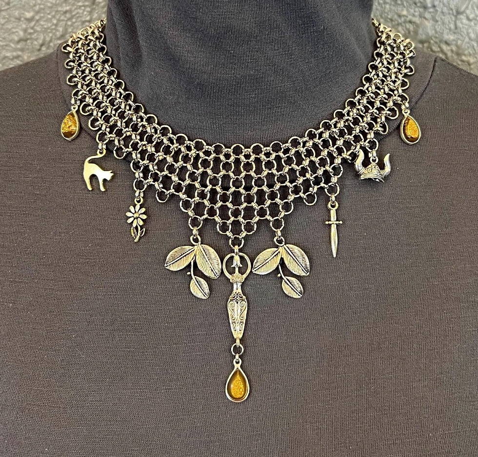 Close-up of an ornate silver chainmail necklace with dangling charms on a dark turtleneck background, landscape crop.