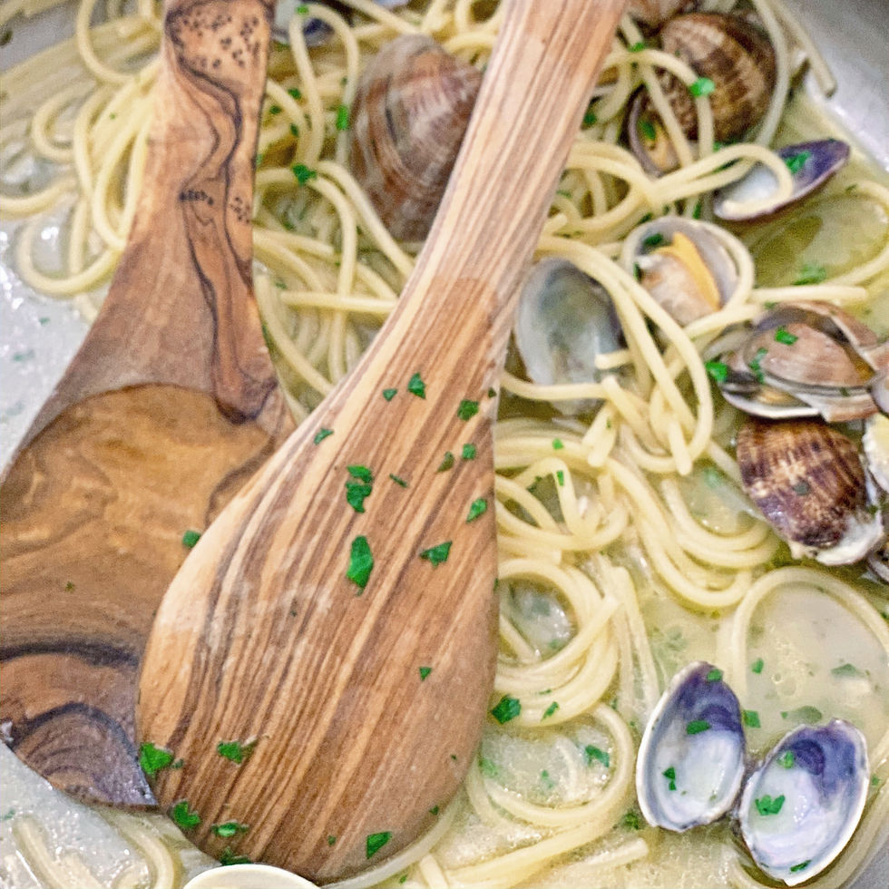 A simple Italian seafood pasta finished with fresh clams, olive oil, and herbs, served with rustic wooden utensils.