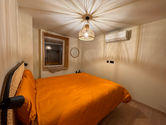 Chambre double avec lit double, draps ocre, fenêtre, lampe au milieu du plafond et appareil pour climatisation