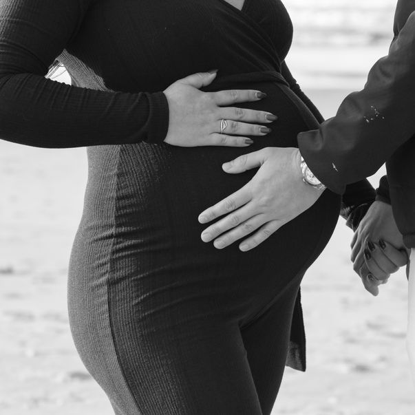 Een zwart-wit foto van het strand en met zwangere vrouw en man die handen op de buik leggen. 