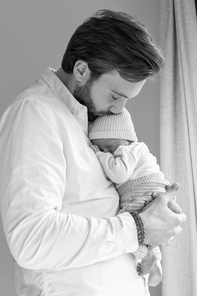 Een zwart-wit foto met een vader en pasgeboren baby. De vader draagt de baby en geeft hem een kusje op zijn hoofd. 